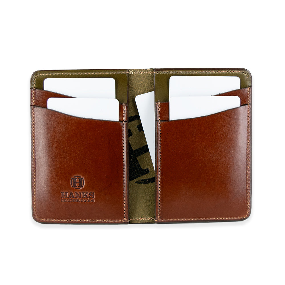 The Superior Front Pocket Bifold by Hanks Belts is an open brown handcrafted wallet made from premium USA harness leather. It has four card slots, each holding a white card, a stitched design, "HANKS" embossed on the lower left side, and an olive green interior lining.