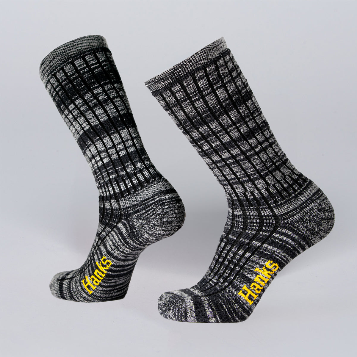 Two black and gray patterned Upland Socks by Hank Belts feature "Hanks" in yellow on the soles, shown against a plain light gray background.
