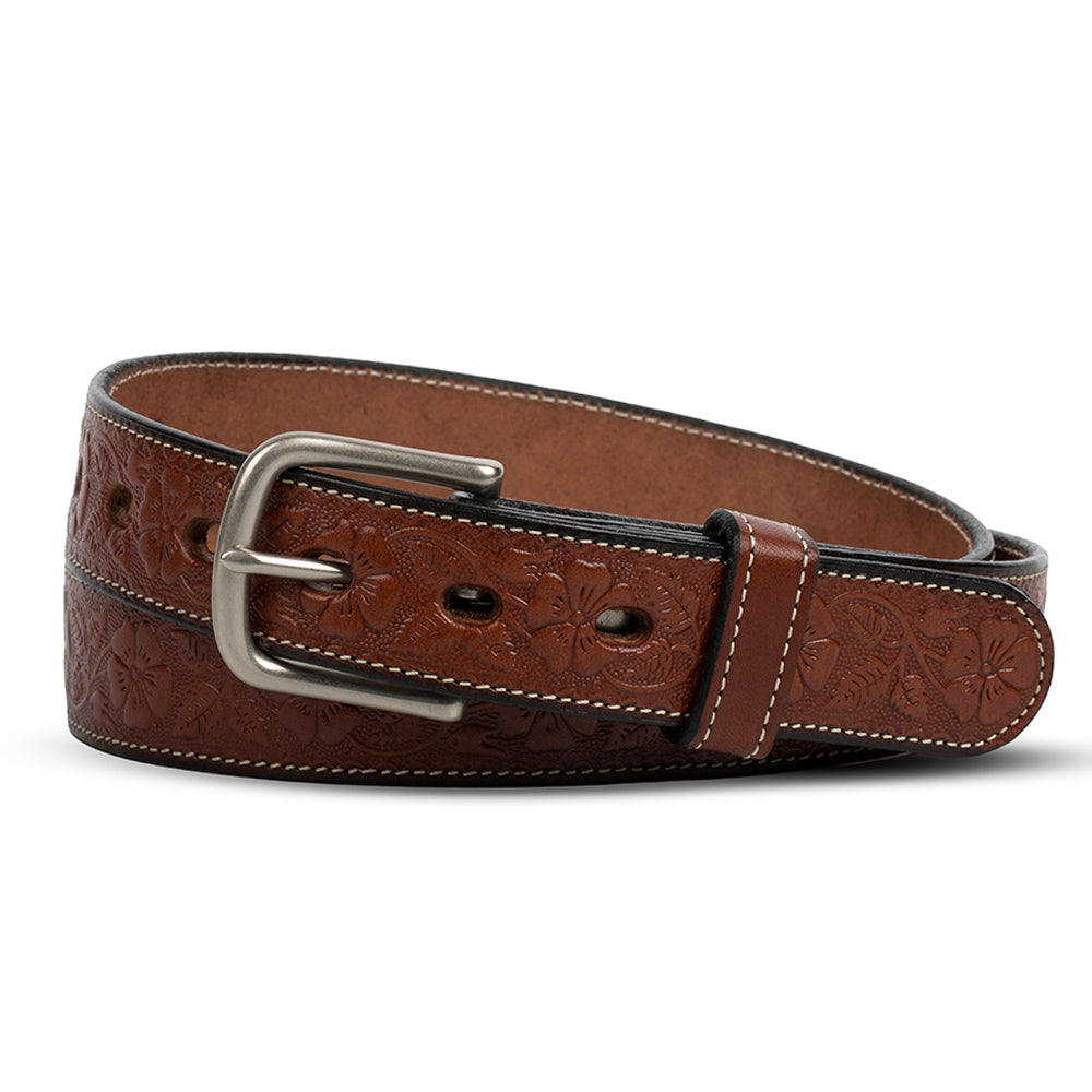 The Hanks Belts Floral Embossed in Oak is a full-grain leather belt with floral embossing, white edge stitching, and a silver rectangular buckle, shown coiled in a loose loop against a white background.