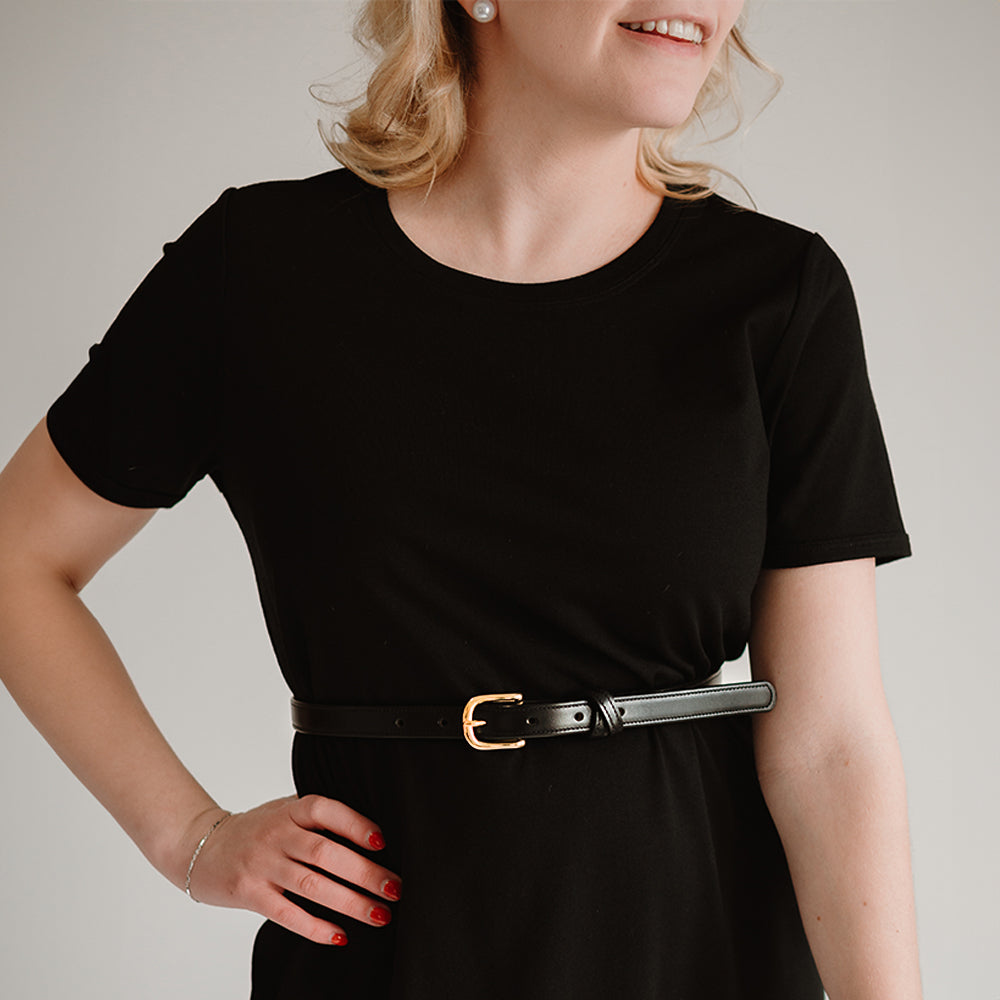 A woman with red nails and wavy blonde hair shines in a black short-sleeve dress, smiling against a plain light background. She wears Hanks Belts' The Dixie, featuring premium English Bridle leather and a gold buckle.