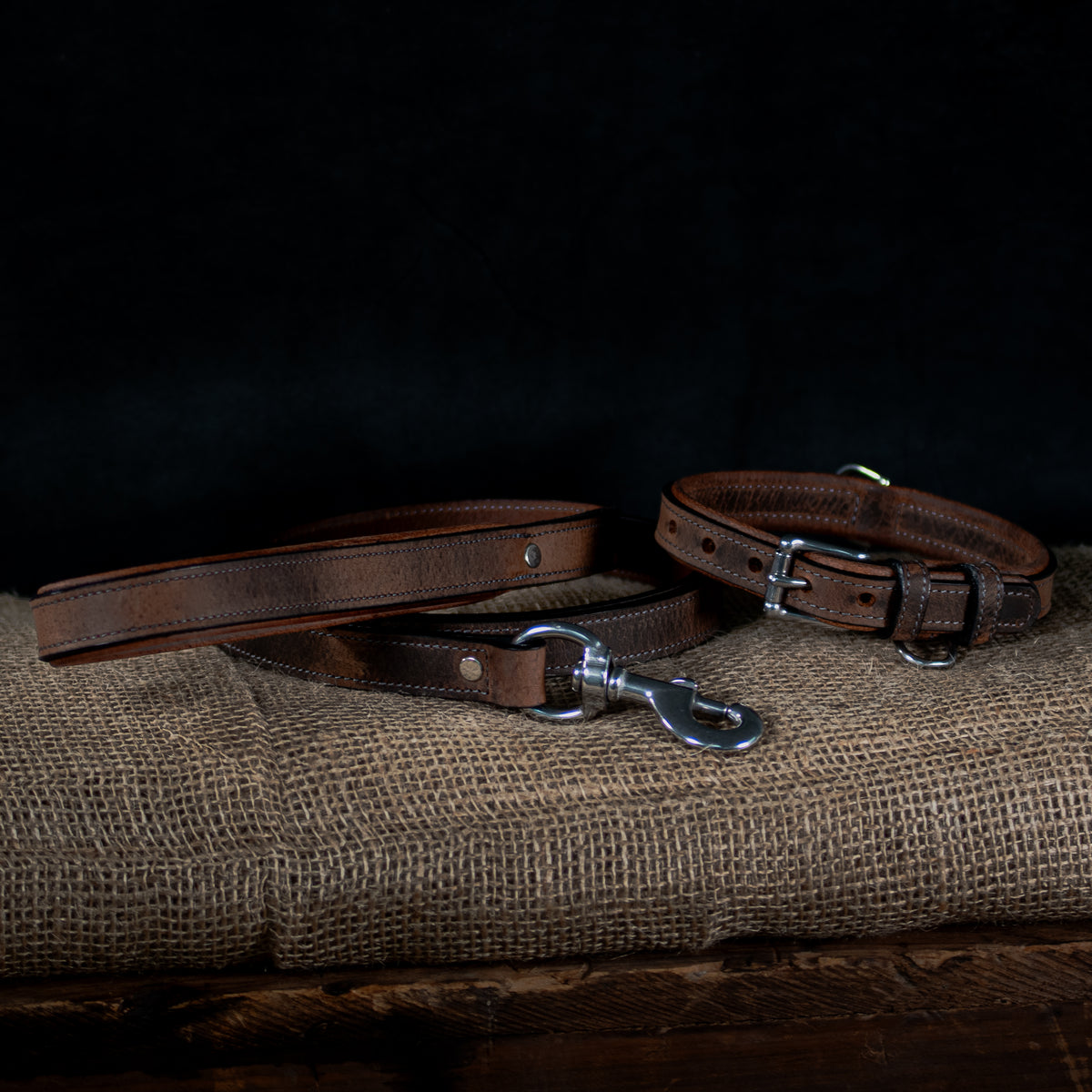 The Hanks Belts Kodak Bison Collar and matching leash, made from premium bison leather with metal buckles, are shown on burlap against a dark background, highlighting their rugged durability and timeless style.