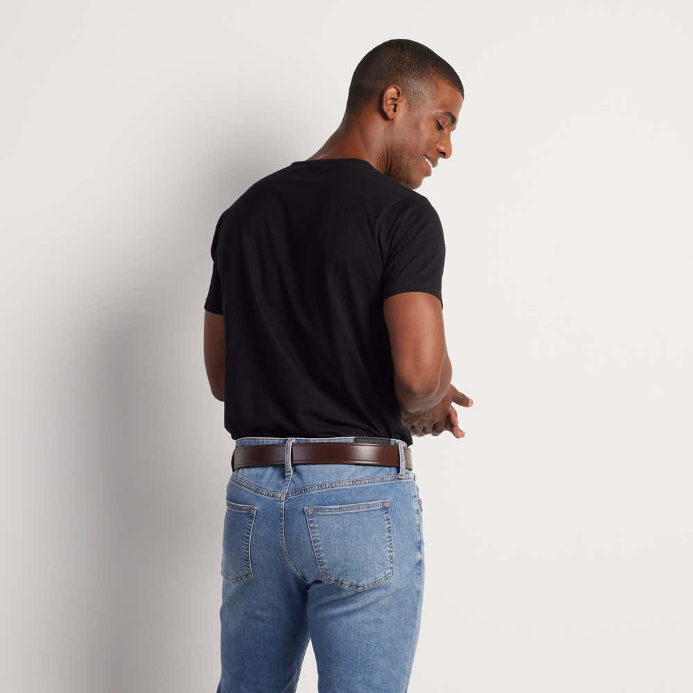 A man faces away from the camera, wearing a black t-shirt, light blue jeans, and the Hanks Belts Sweat & Waterproof Belt Synthetic Double Layer, looking down and to the side against a plain white background.