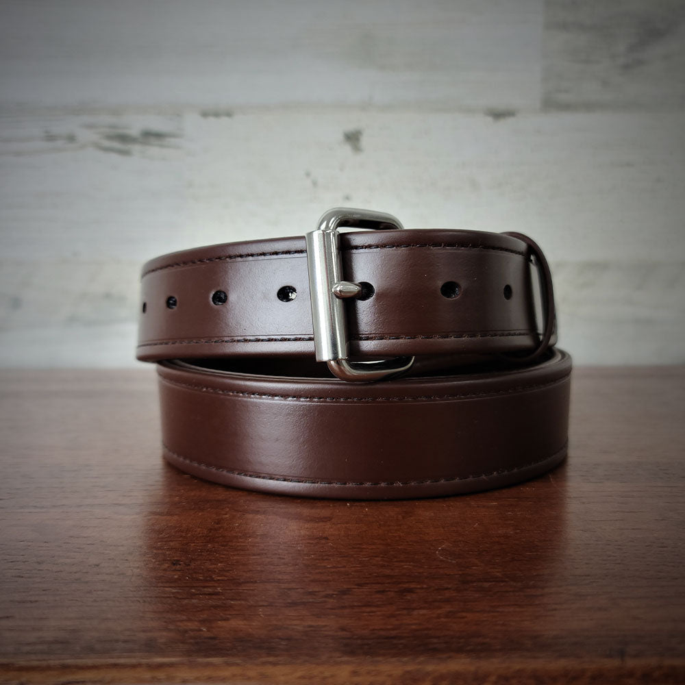 The Hanks Belts Sweat & Waterproof Belt Synthetic Double Layer, featuring a dark brown design and silver buckle, is coiled neatly on a wooden surface against a light, textured background.