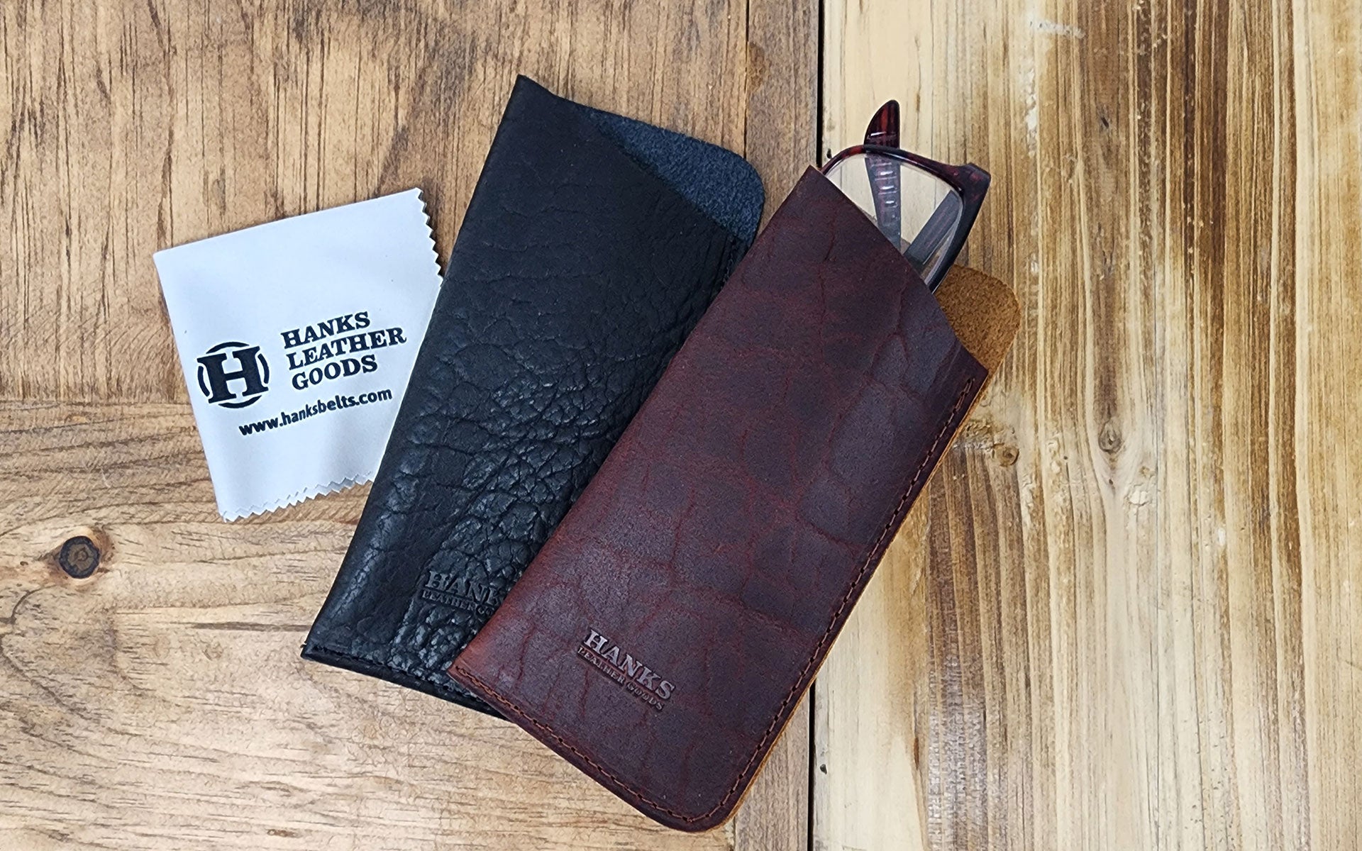 Black and Brown Bison eyeglass cases with glasses in the case and cleaning cloth next to the cases on wooden backgrouond