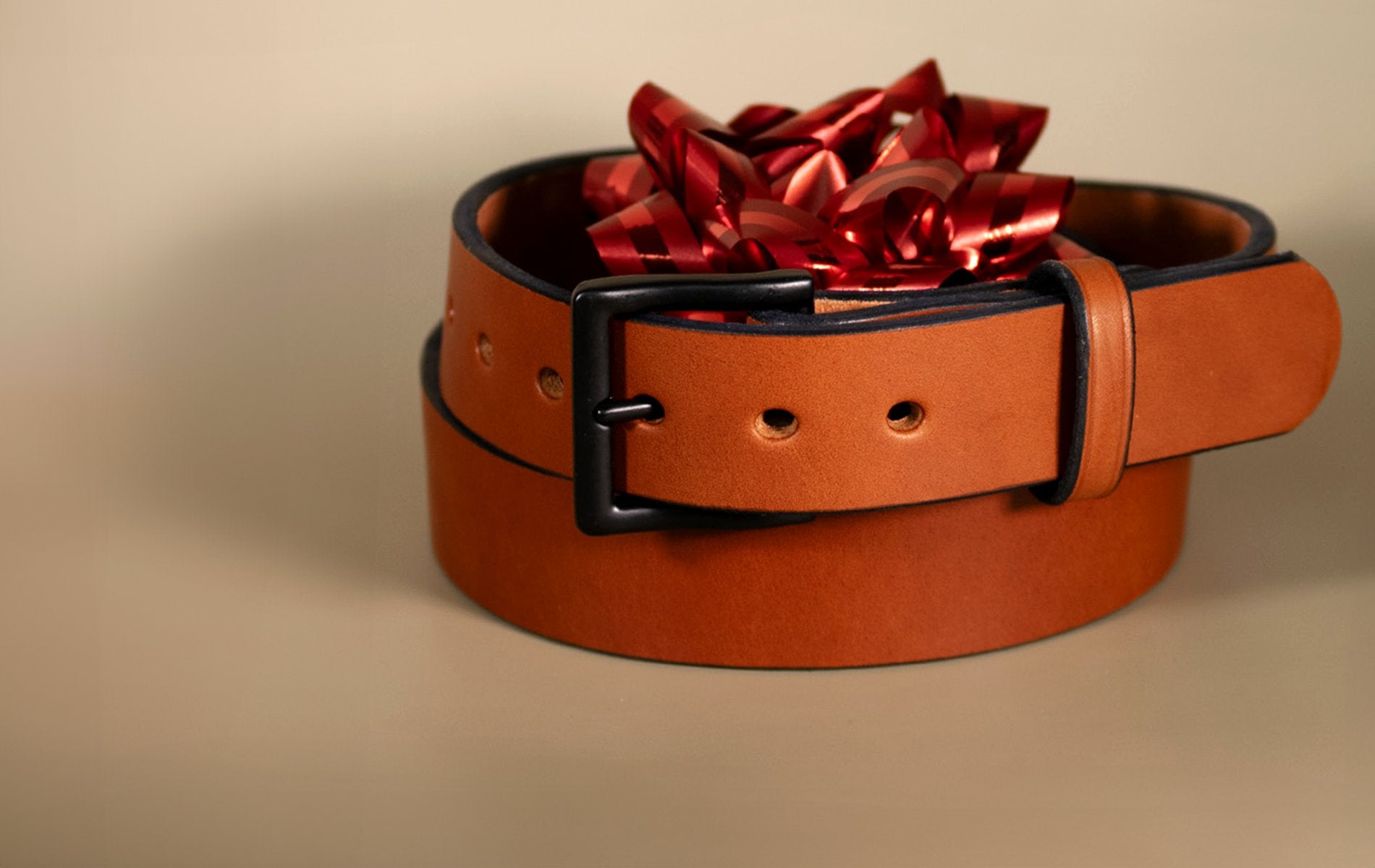 Hanks Everyday belt with red bow on rolled up top on tan backdrop