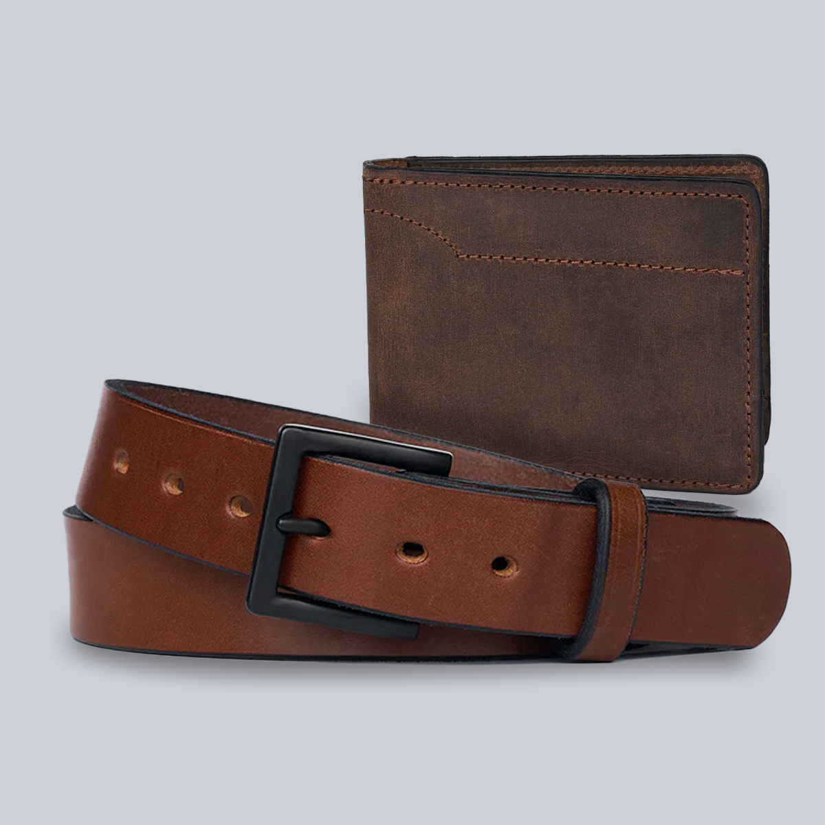 The Hanks Belts Bundle: Everyday Belt with black metal buckle and Tahoe Bifold Wallet, both in brown leather, are displayed coiled together against a plain gray background.