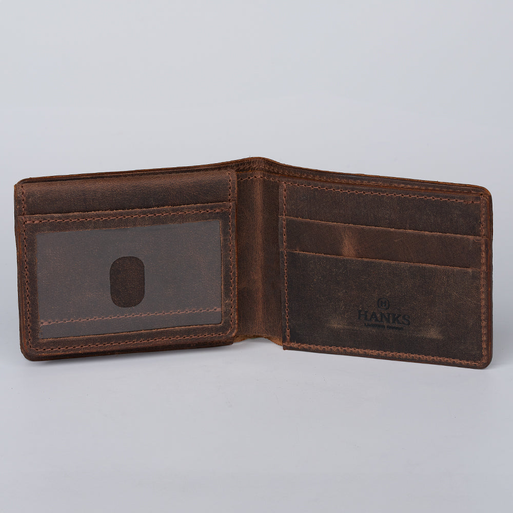 An open Hanks Belts Grainmark Line Bifold with ID Window in brown leather features visible card slots, a left-side transparent ID window, and an embossed Hanks logo inside right. The empty wallet is photographed on a light gray background.