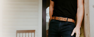Person wearing a black t-shirt and dark jeans with a brown belt, standing indoors.