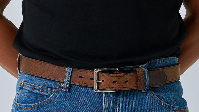 Person wearing a brown belt with a black shirt and blue jeans on a light gray background