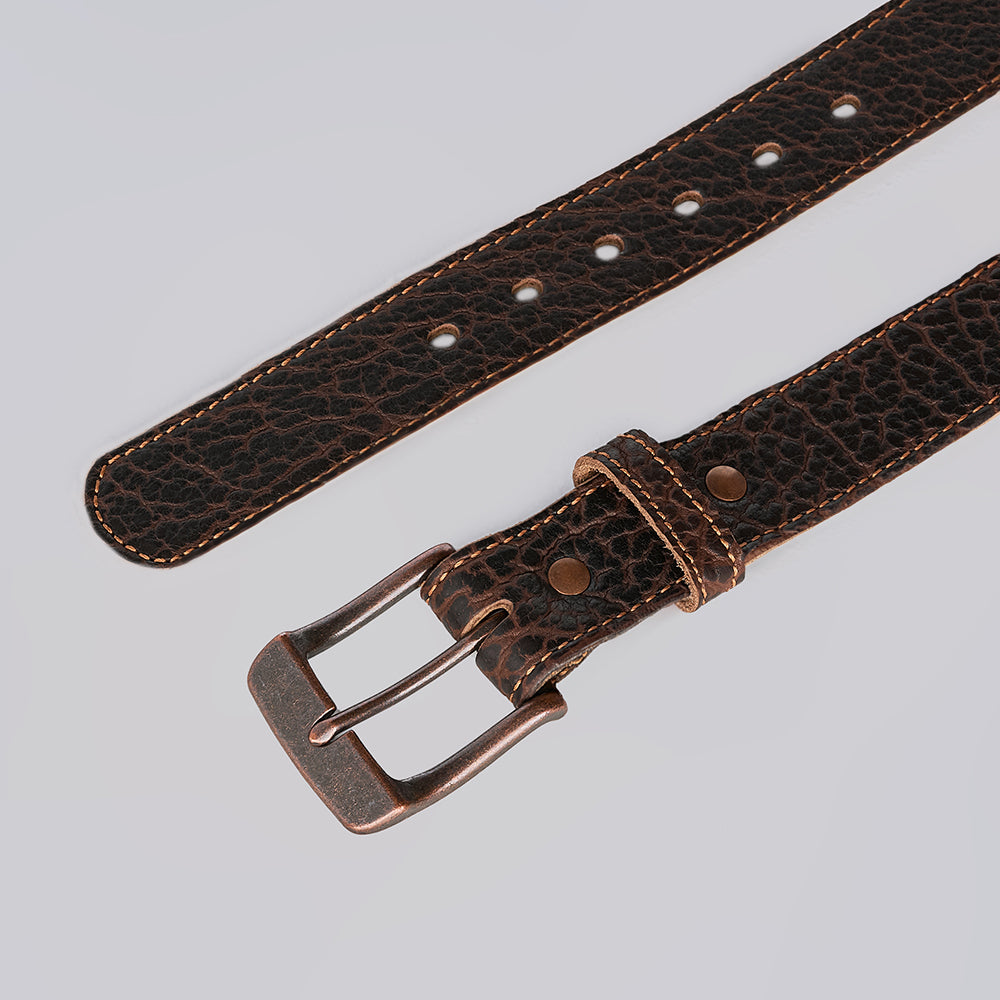 A close-up of the Hanks Belts Bison Bellow, a dark brown textured leather belt with light brown stitching and a rectangular metal buckle, laid flat on a light gray background.