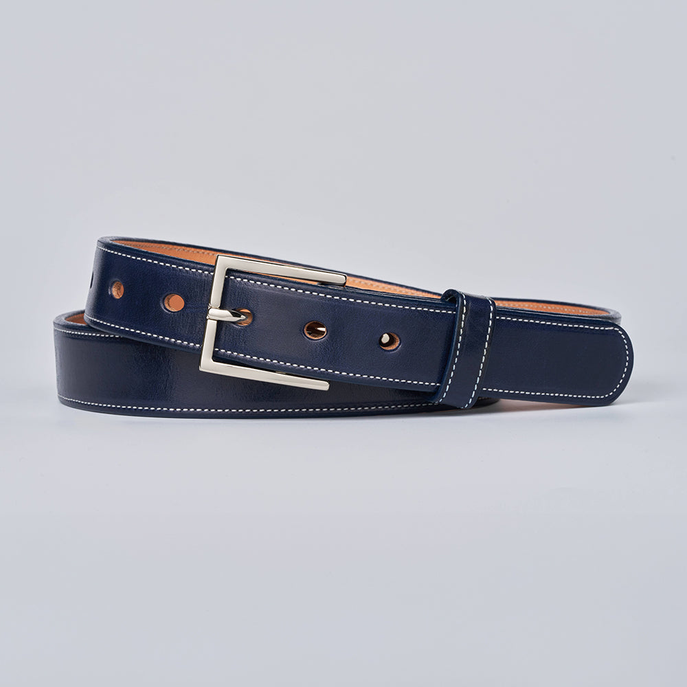 The Midnight Ranger by Hanks Belts is a navy blue English Bridle Leather belt with white stitching and a silver rectangular buckle, coiled neatly on a light gray background.