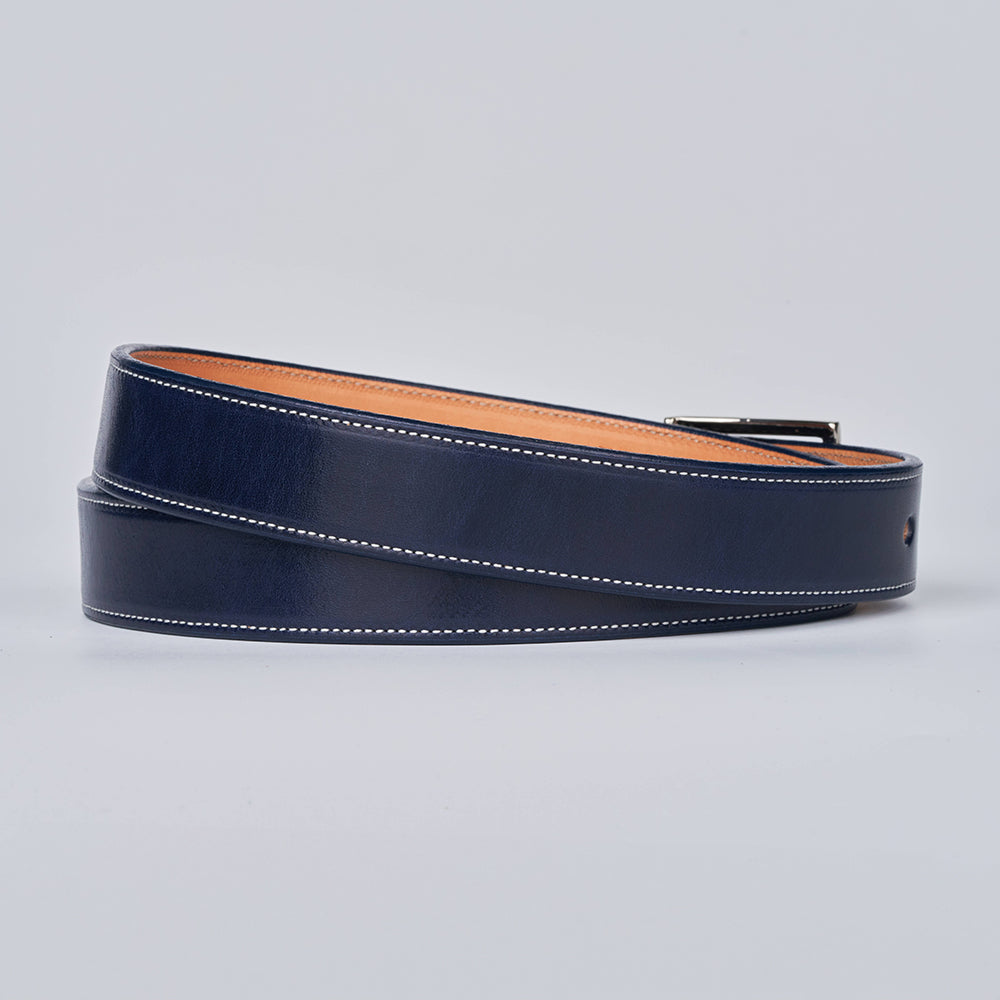 The Midnight Ranger by Hanks Belts is a navy blue premium harness leather belt with white stitching, a tan-colored inner side, and a partially visible metal buckle, neatly coiled on a light gray background.