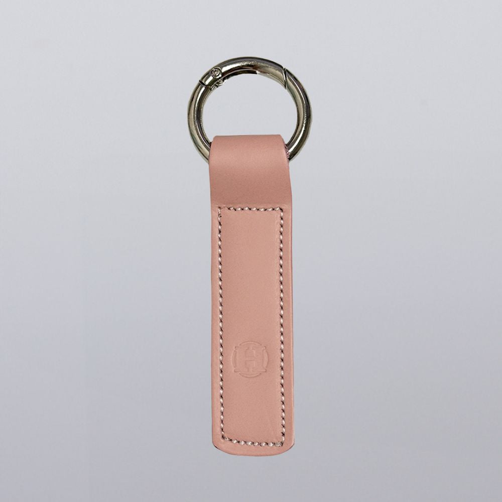 The Hanks Belts Superior Keychain is a pink leather rectangle with edge stitching, a silver open gate keyring, and an embossed logo near the bottom, shown against a light gray background.