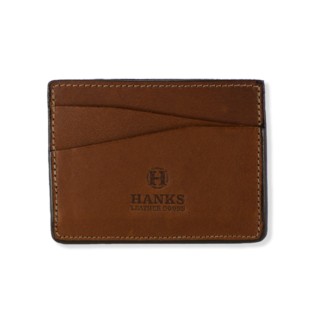 Introducing the Cumberland Bison Card Holder by Hanks Belts: a peanut brown leather card holder crafted from durable Bison Leather, showcasing the brand name "Hanks Leather Goods" with an embossed logo on the front. This ultra-thin, lightweight wallet is made in the USA and features two slanted card slots along with visible stitching along the edges for a timeless look.