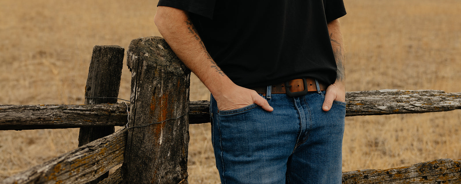Male model wearing Hanks Relic Belt leaning up a wooden fence outdoors