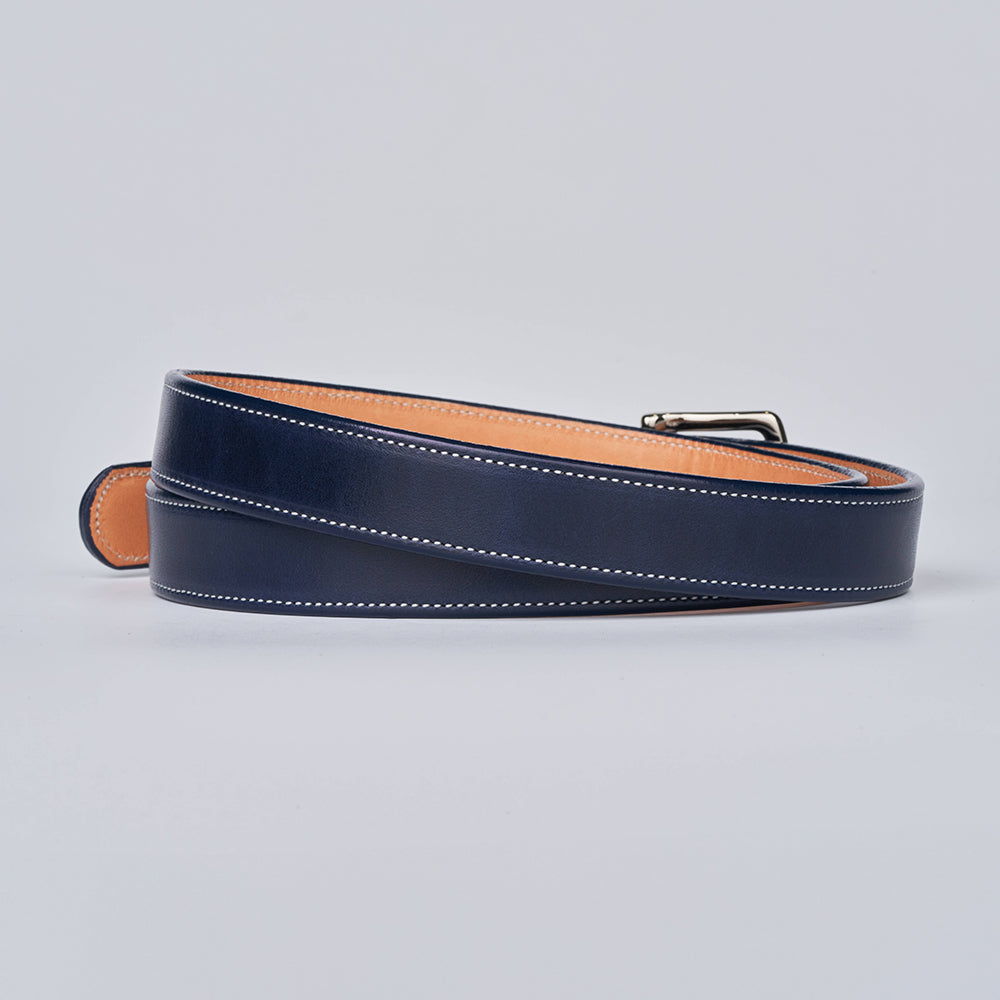 A limited-edition Hanks Belts Midnight Grace - 1&quot; navy belt in dark blue vegetable-tanned leather with white edge stitching and a silver buckle, shown rolled up on a light gray background.