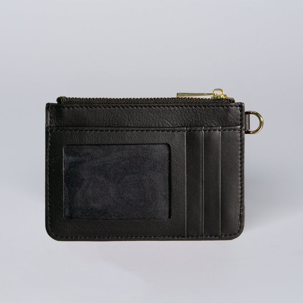 The Hanks Belts Livia Mini Wristlet is a black leather cardholder with three card slots, a clear ID window, zippered compartment, and gold-tone key ring, shown on a plain light gray background.