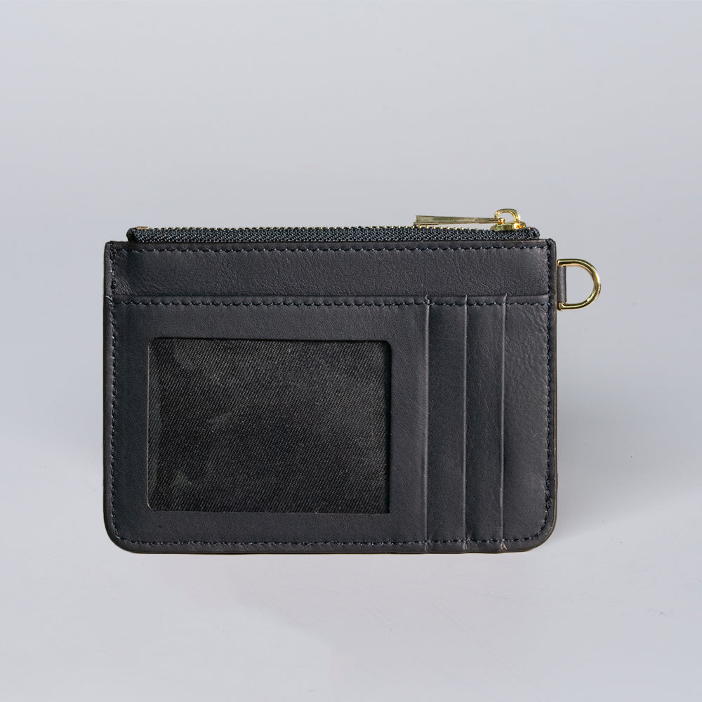 The Hanks Belts Livia Mini Wristlet is a black leather card holder with a clear ID slot, three card slots, top zipper compartment, and gold keyring attachment, shown against a light gray background.