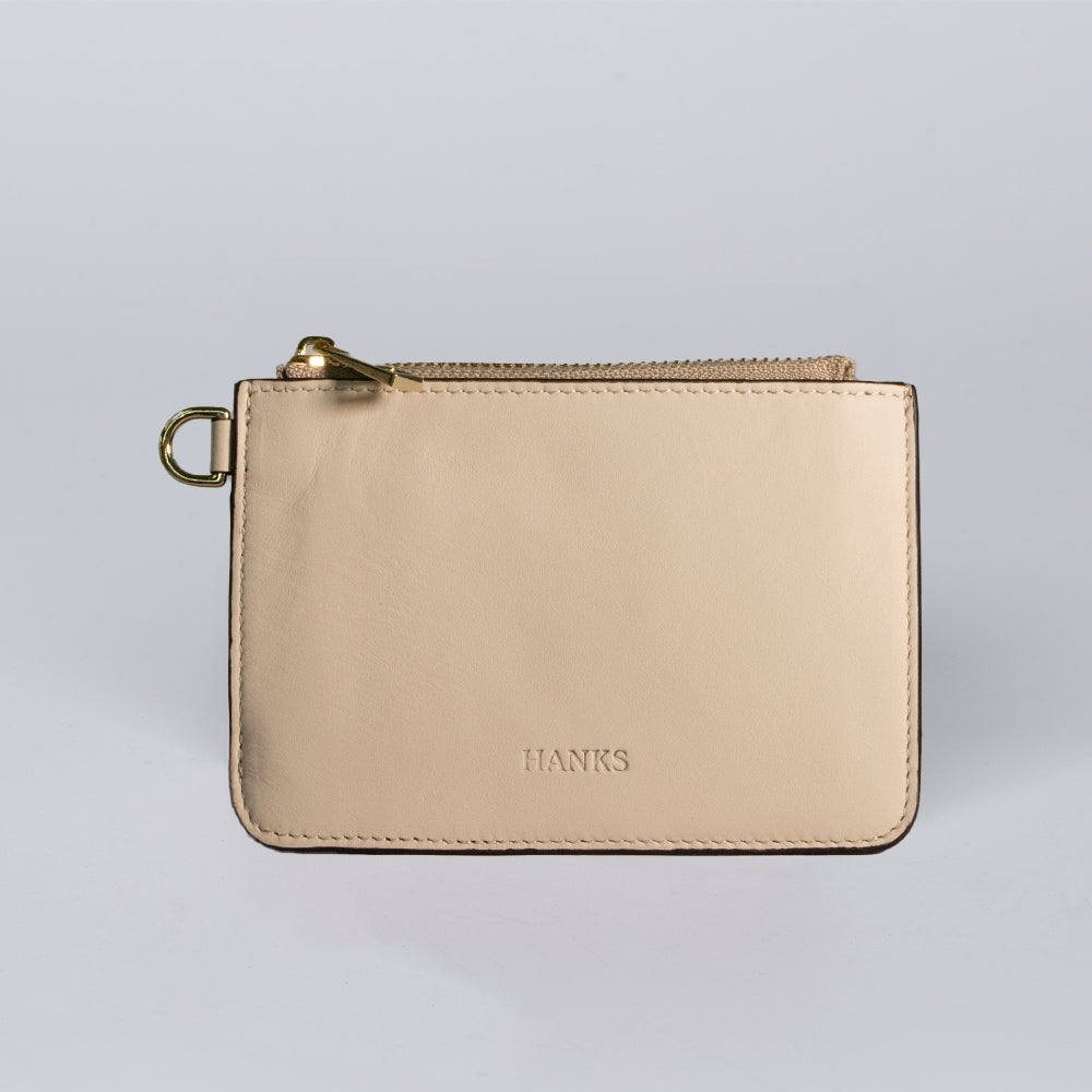 The Livia Mini Wristlet by Hanks Belts is a beige leather pouch with gold hardware and "HANKS" embossed on the front, shown against a plain light background.