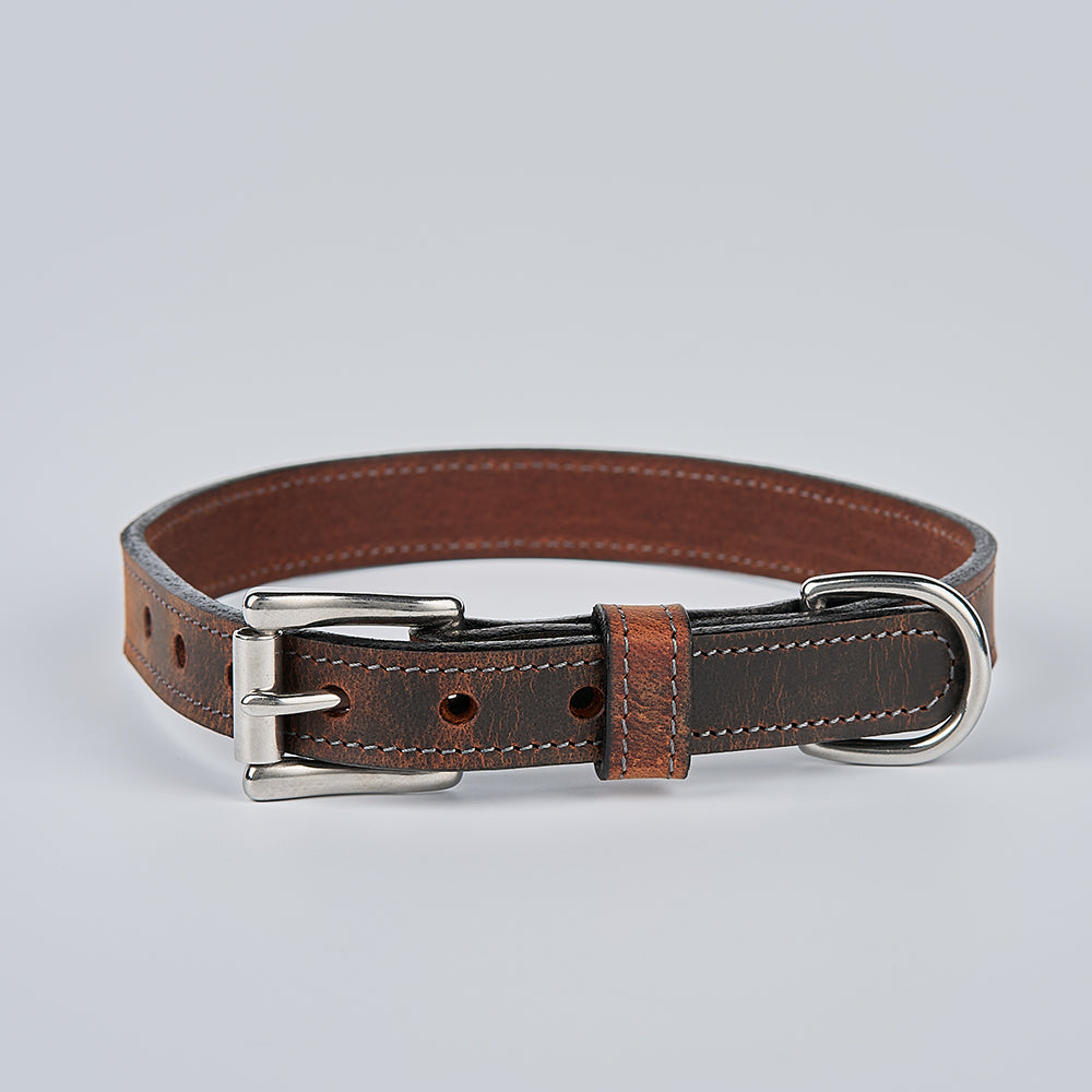 The Ollie Bison Collar by Hanks Belts is a stylish brown leather dog collar featuring a metal buckle and D-ring, shown on a light gray background.