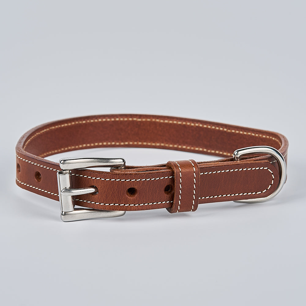 The Ollie Bison Collar by Hanks Belts, a brown leather dog collar with white stitching, silver buckle, and D-ring, is shown on a simple light gray background.