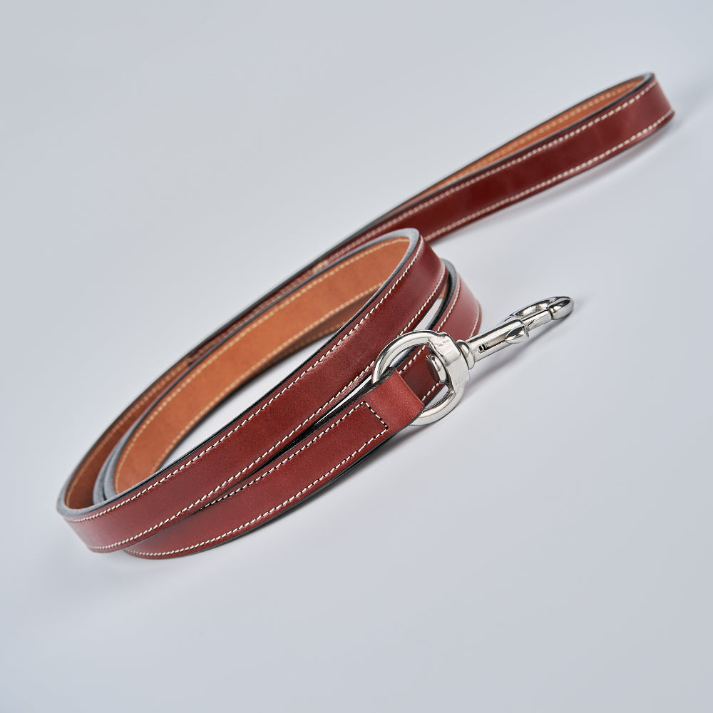 The Old Reliable Leash by Hanks Belts, crafted from brown English bridle leather with white stitching and a silver clasp, is shown coiled neatly on a light gray background.