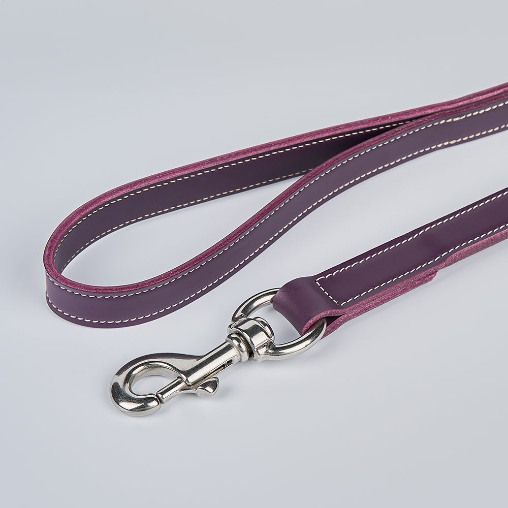 A close-up of the Old Reliable Leash by Hanks Belts, made from purple English bridle leather with white stitching and a silver clasp, displayed on a plain light gray surface.
