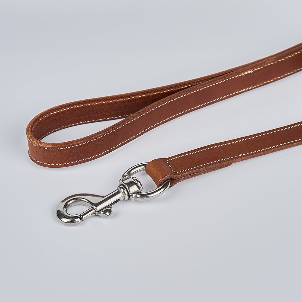 The Ollie Bison Leash by Hanks Belts, crafted in the USA from premium bison leather with white stitching and a silver metal clasp, is coiled on a light grey surface to highlight its durability and quality craftsmanship.