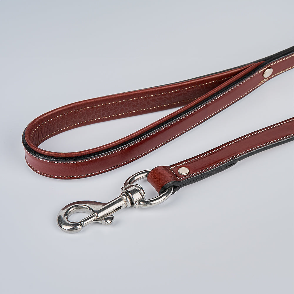 The Hanks Belts Rover Standard Leash, crafted from brown English bridle leather with white stitching, a padded loop handle, and a silver clasp, is shown on a light gray surface.