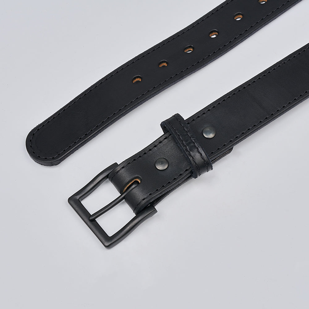 A close-up of Hanks Belts&#39; The Black Out Tactical shows its matte black rectangular buckle and metal rivets on extreme leather, with multiple holes for size adjustment, displayed on a light gray background.