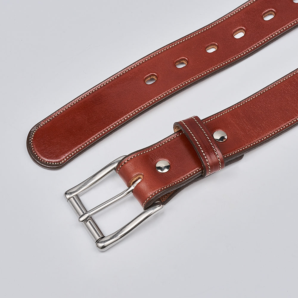 The Canyon by Hanks Belts is a handcrafted English bridle leather belt with white stitching, a silver buckle, and multiple adjustment holes, shown on a light gray background.