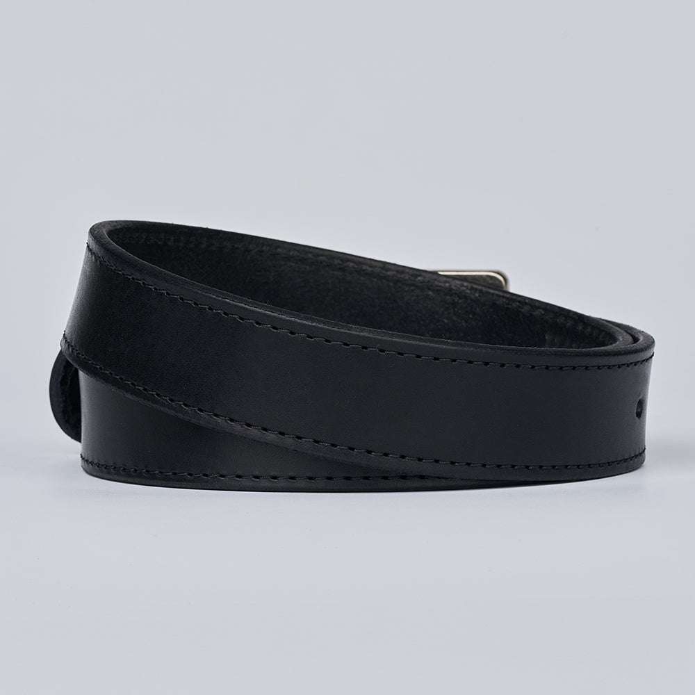 The Double Roller by Hanks Belts—a coiled black full-grain leather belt with visible stitching and a partially hidden metallic buckle—rests on a light gray background.