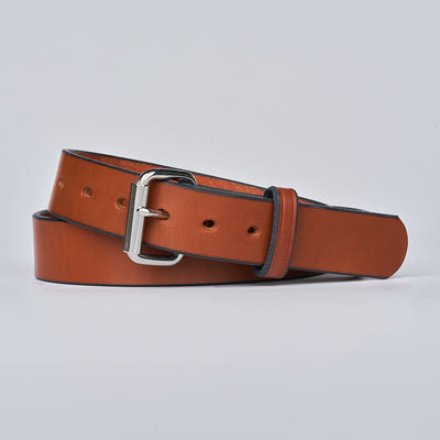 The Gunner by Hanks Belts, a brown leather CCW belt with a silver buckle, is rolled up and displayed on a plain light gray background.