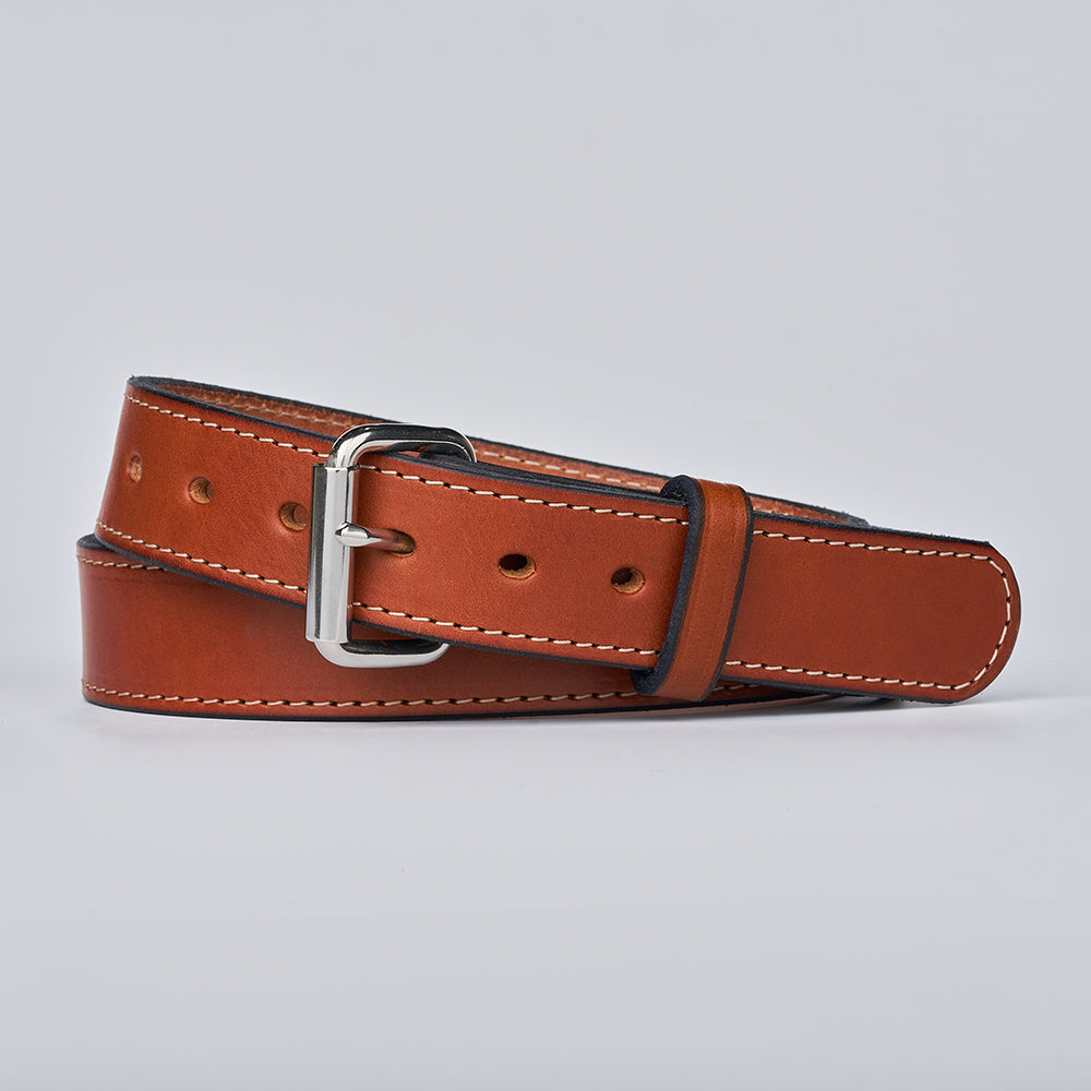 The Gunner Stitched by Hanks Belts: a brown full-grain leather belt with white stitching and a silver buckle, neatly rolled on a light gray background.