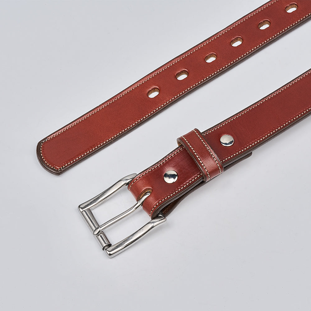 The Highland Lined by Hanks Belts is a brown premium leather belt with white stitching, a silver double-prong buckle, and multiple holes, displayed on a light grey background.