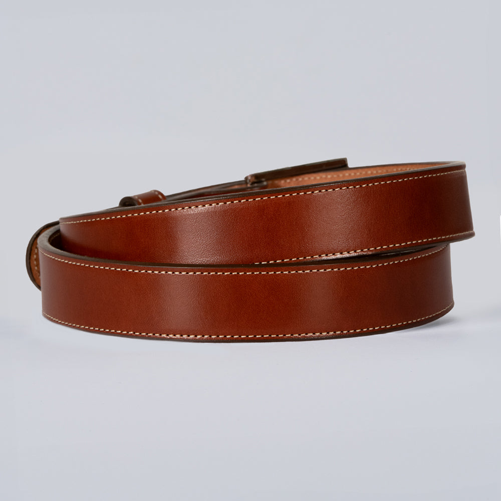 The Ledger by Hanks Belts, a brown leather belt with white stitching, is coiled neatly against a plain light gray background.