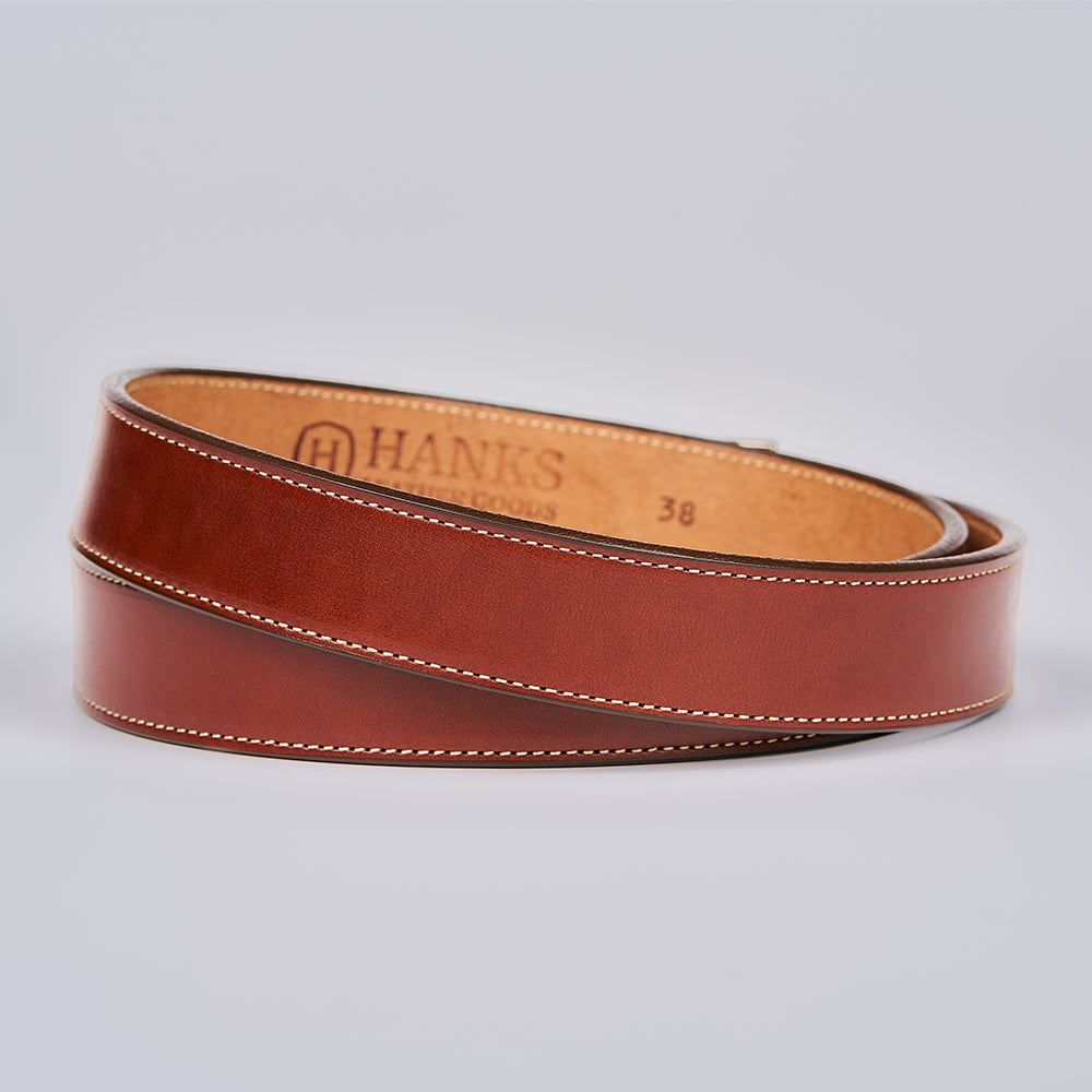 The Ledger by Hanks Belts, a brown English bridle leather men's dress belt with white stitching, is coiled on a light grey background. The inner side features brand marking and the size "38" imprinted on it.