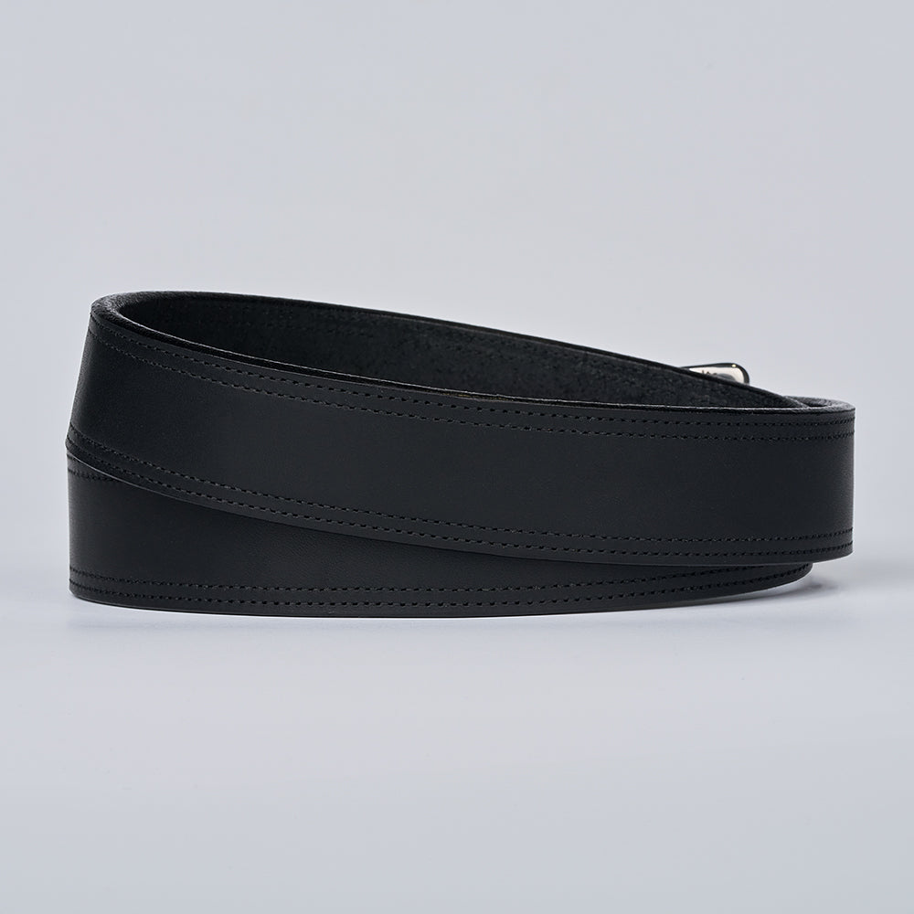 The Old World Harness by Hanks Belts, a black full-grain leather belt with subtle diagonal stitching, is coiled neatly on a plain light gray background.