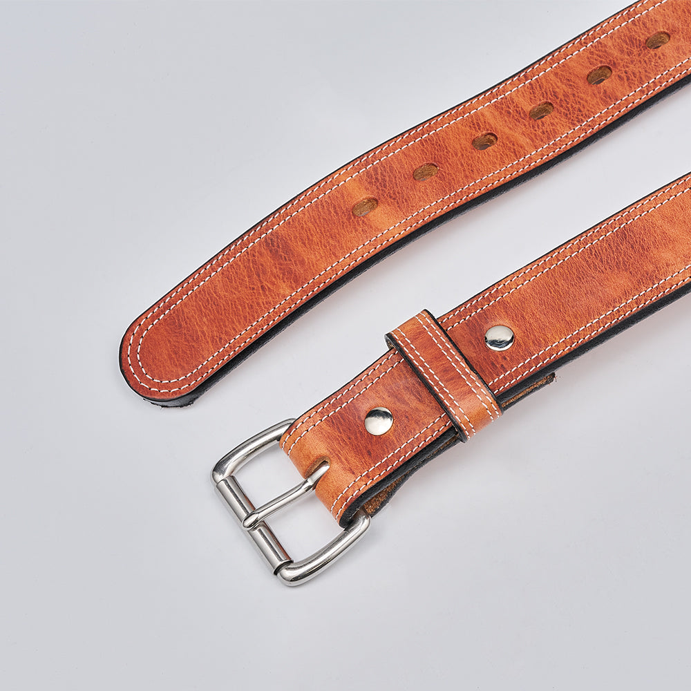 The Hanks Belts Old World Harness is a brown full-grain leather belt with white stitching, multiple holes, and a silver buckle, made from USA-tanned Hermann Oak leather, shown on a light gray background.