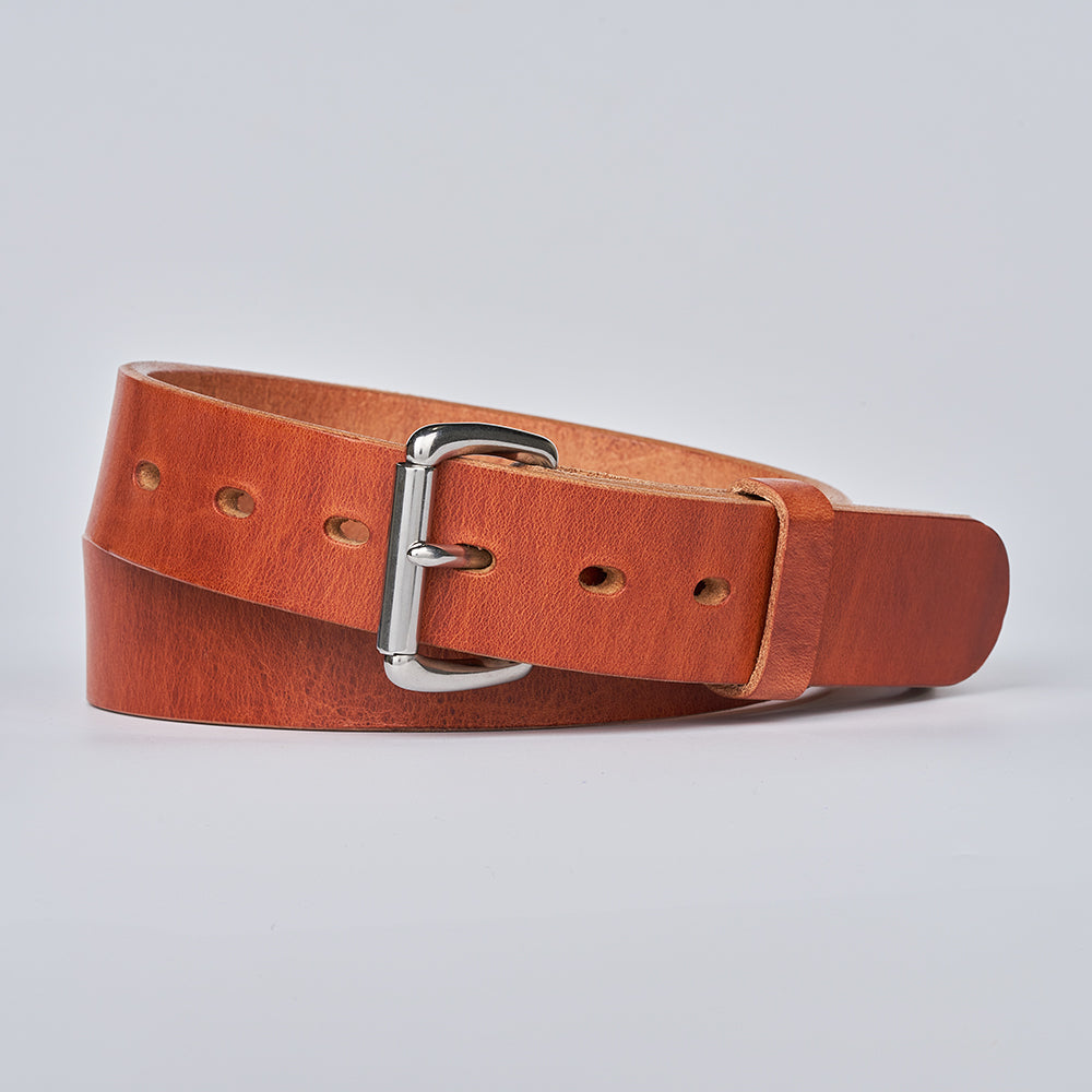 The Old World Harness by Hanks Belts, made from premium USA-tanned Hermann Oak full-grain leather and finished with a silver buckle, is rolled up and showcased against a plain light gray background.