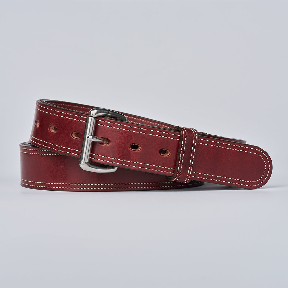 The Premier Double Layer by Hanks Belts—a coiled brown English bridle belt made from vegetable tanned leather with white stitching and a silver buckle—is displayed on a plain light background.