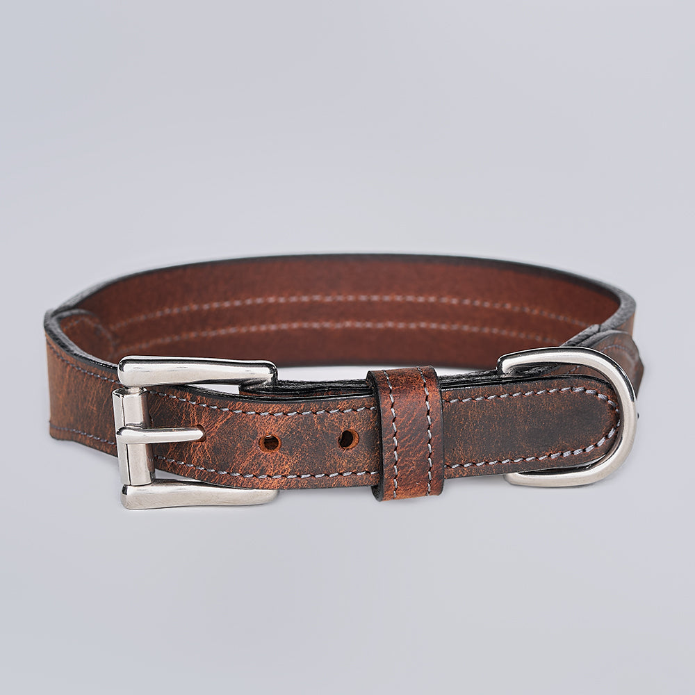 The Remi Reflective Collar by Hanks Belts, made of brown leather with a silver metal buckle and D-ring, is displayed on a light gray background.