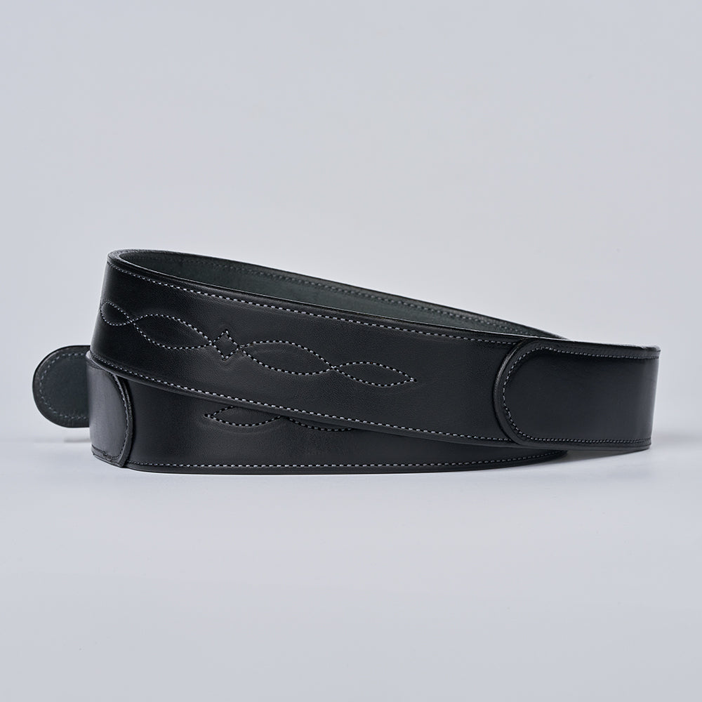 The Teton Tapered by Hanks Belts is a black vegetable-tanned leather guitar strap with decorative white stitching, shown coiled on a plain light gray background.