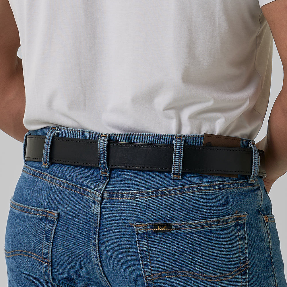A person wears a white t-shirt tucked into blue jeans with The Black Out Tactical belt by Hanks Belts. The photo focuses on the back view, highlighting the waist, belt loops, and back pockets of the jeans.