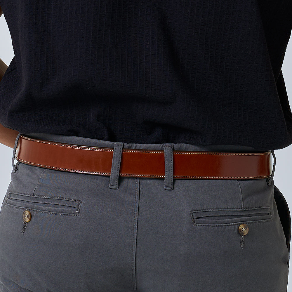 A person wearing a dark shirt, grey pants with back pockets, and The Canyon handcrafted vegetable-tanned leather belt by Hanks Belts with visible stitching. The image centers on the waist and lower back.