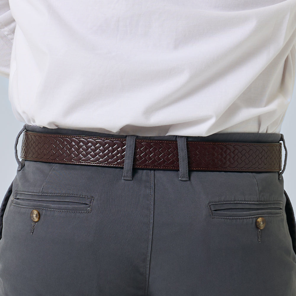A person wears a white shirt tucked into gray pants with buttoned back pockets, showcasing Hanks Belts&#39; The Classic Basket Weave full-grain leather belt in a brown basket weave design from the back view.