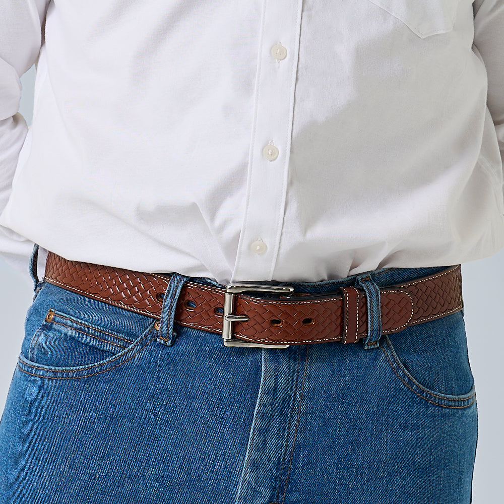 A person wearing blue jeans, a white button-down shirt, and Hanks Belts&#39; The Classic Basket Weave brown leather belt with a silver buckle. The image is cropped to show only the torso and waist.