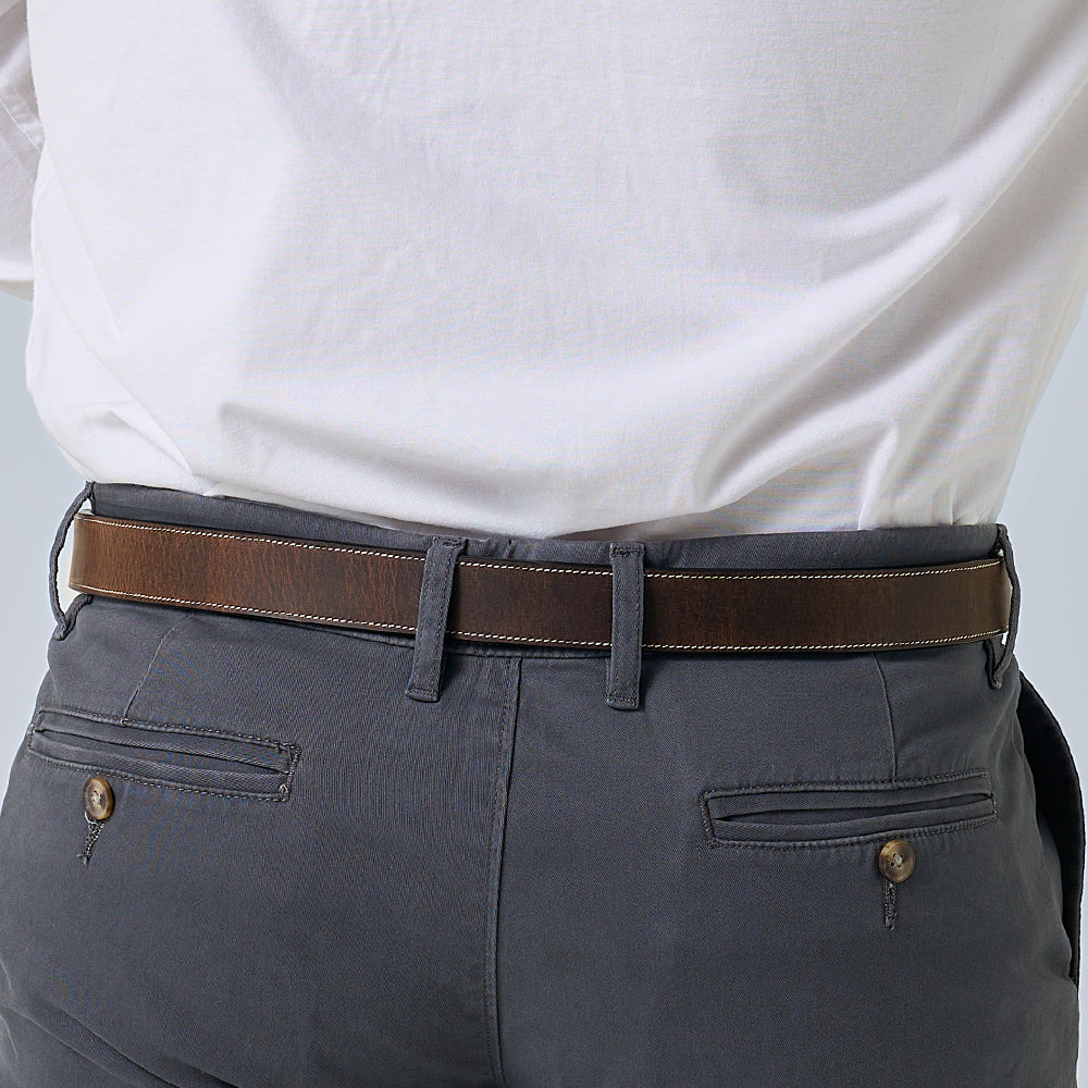A person wears gray pants with buttoned back pockets, a white shirt tucked in, and The Dakota Bison belt by Hanks Belts with a floral buckle. The image focuses on the waist and lower back area.