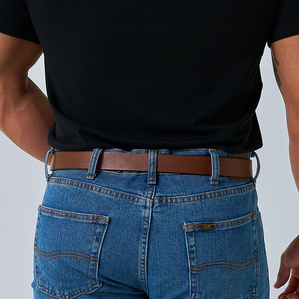 Wearing a black t-shirt, blue jeans, and The Deputy brown leather gun belt by Hanks Belts, a person is seen from the back with hands on hips.