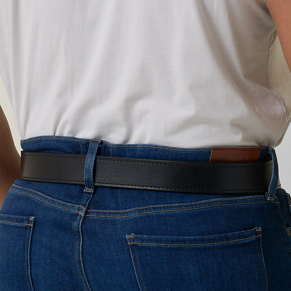 A person in blue jeans and a white shirt, seen from the back, wears Hanks Belts&#39; The Double Roller—a black full-grain leather work belt made in the USA—with a brown patch on the back of the jeans.